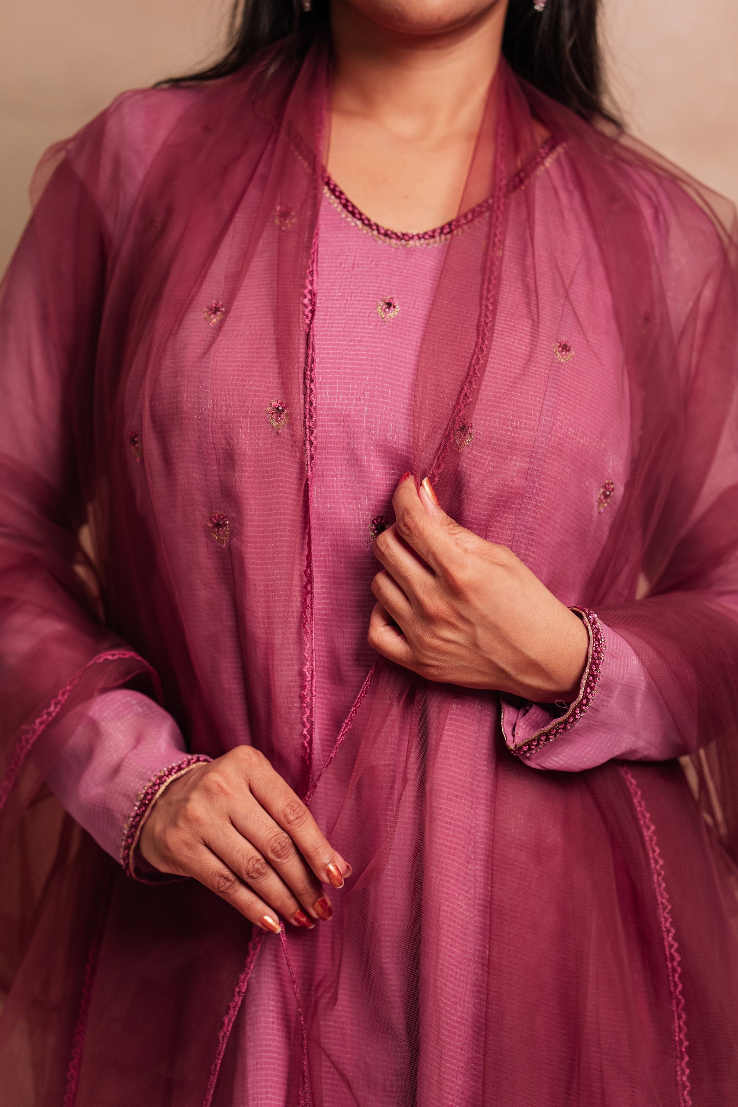 Model Dolly Aishwarya posing for closeup detailing in a hand embroidered tissue chiffon salwar set in onion pink paired with a tulle dupatta by team AKloset.