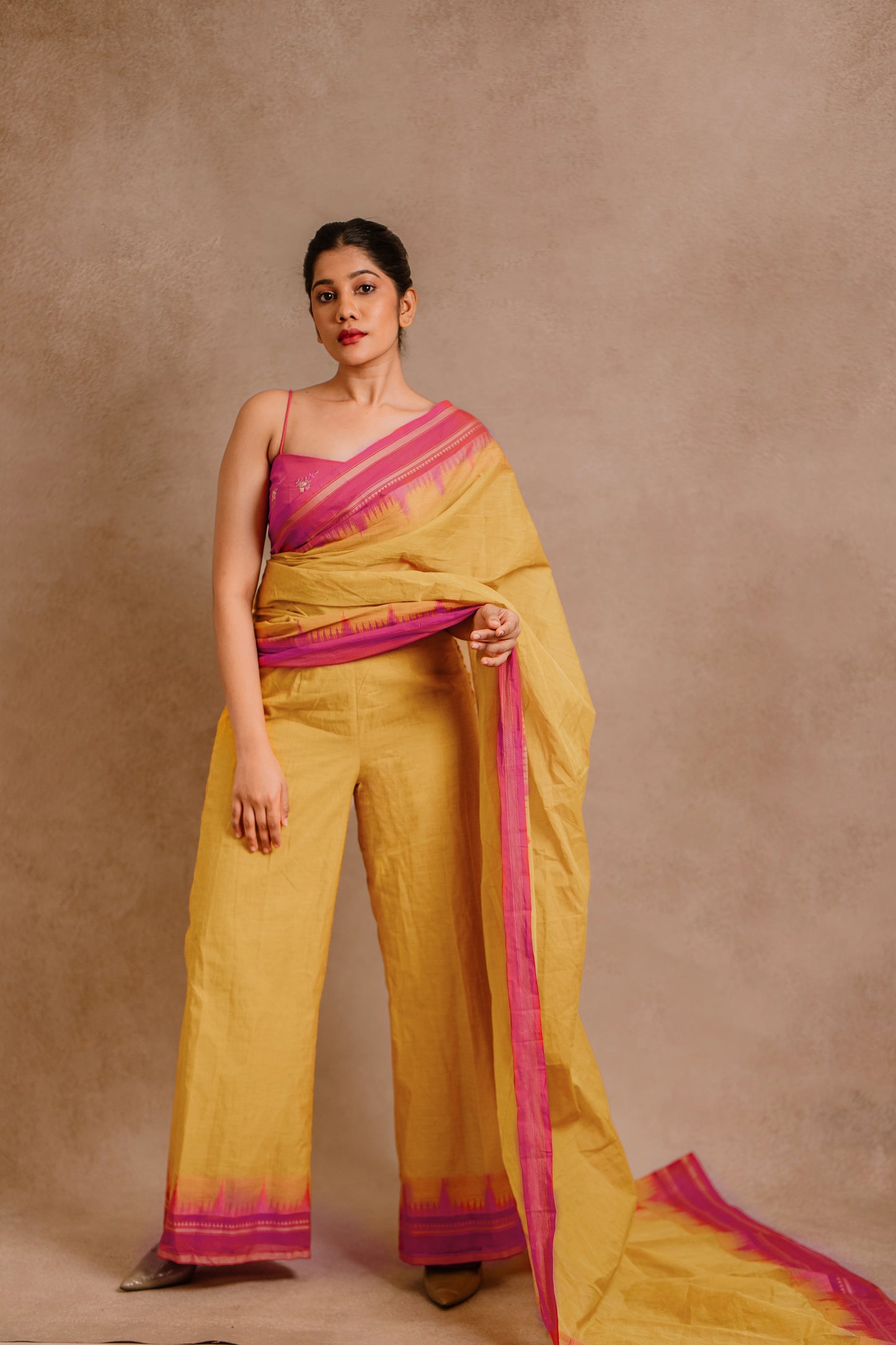 Model Jaina Parmar posing in a draped pant saree in yellow paired with a hot pink spaghetti strap blouse by team AKloset.
