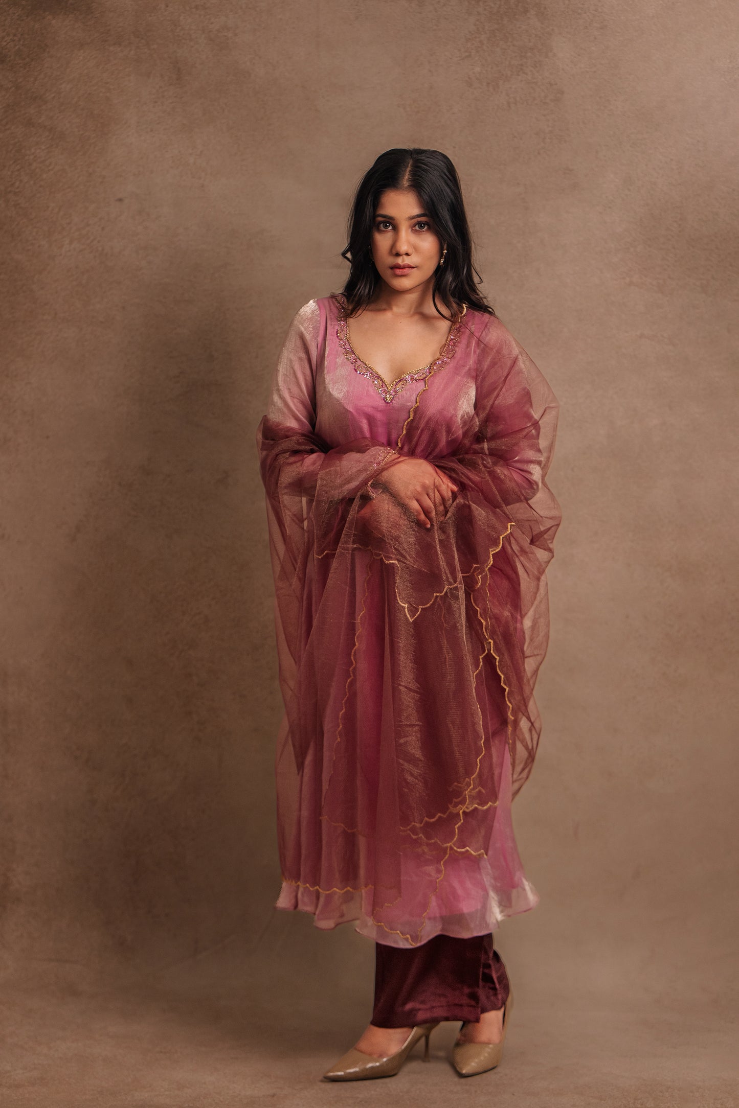 Model Jaina Parmar posing looking at the lens in a hand embroidered tissue chiffon anarkali in onion pink (dual tone), paired with an embroidered tulle dupatta in wine red by team AKloset.