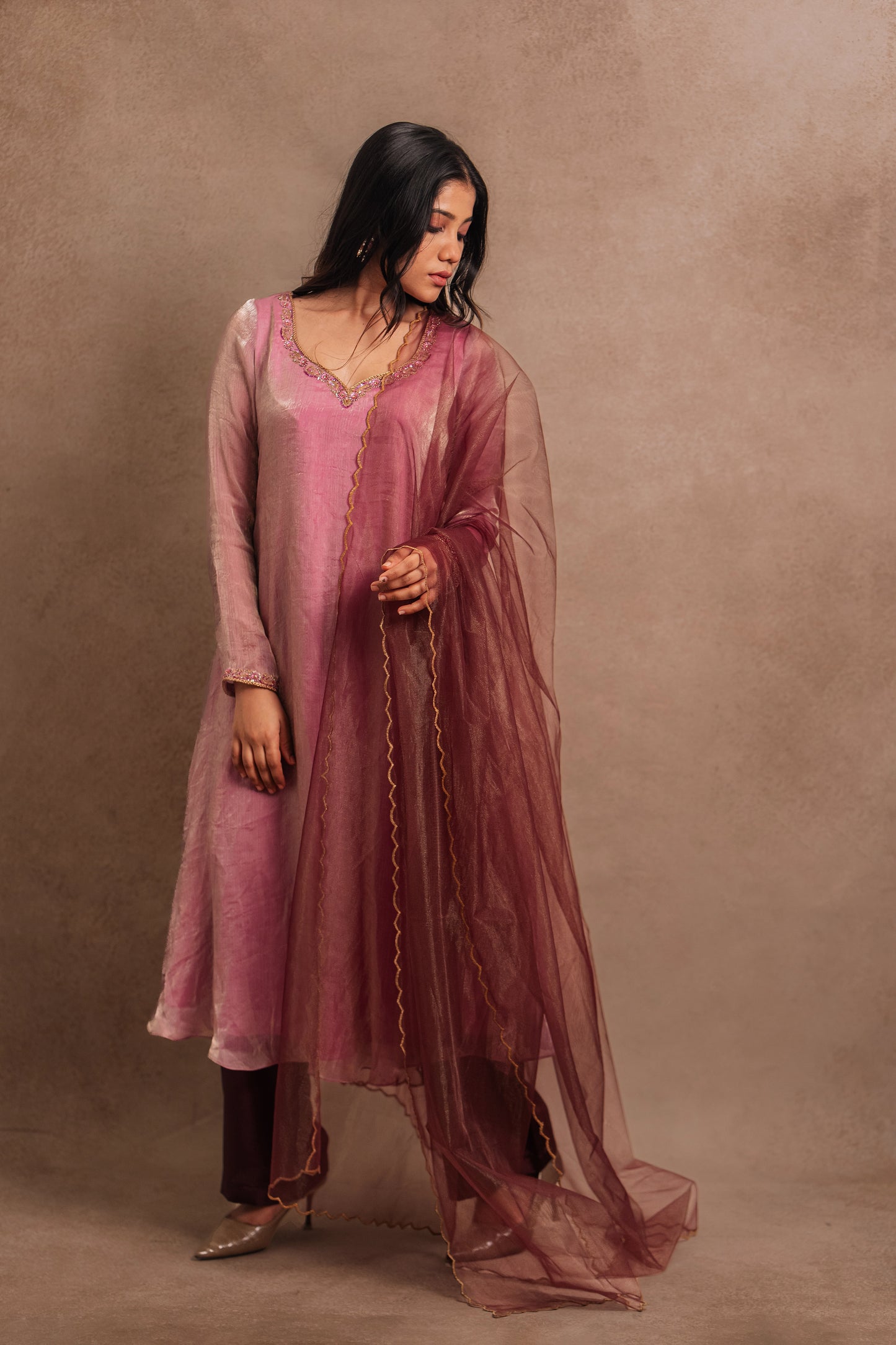 Model Jaina Parmar posing looking down in a hand embroidered tissue chiffon anarkali in onion pink (dual tone), paired with an embroidered tulle dupatta in wine red by team AKloset.