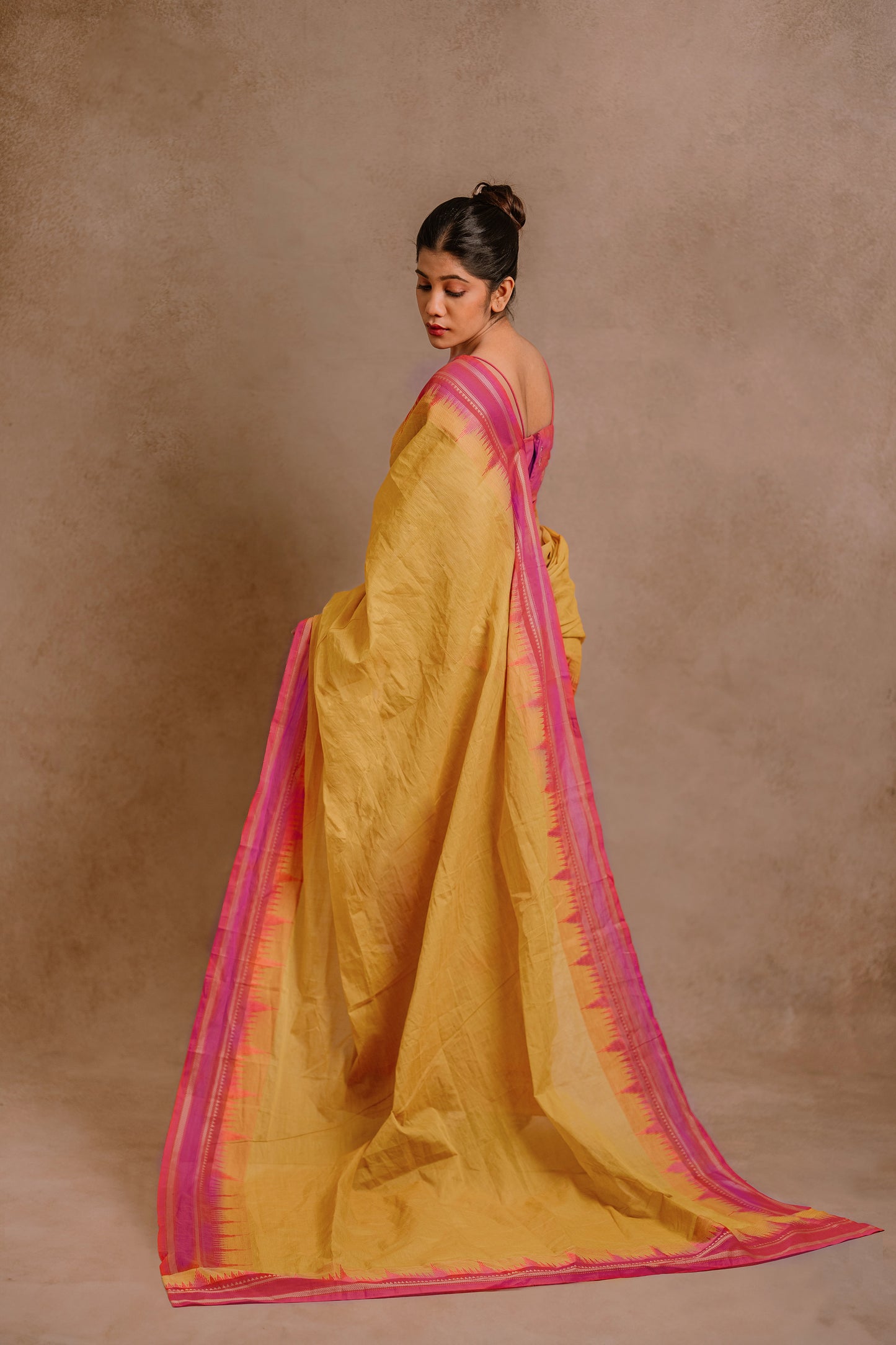 Model Jaina Parmar showcasing pallu in a draped pant saree in yellow paired with a hot pink spaghetti strap blouse by team AKloset.