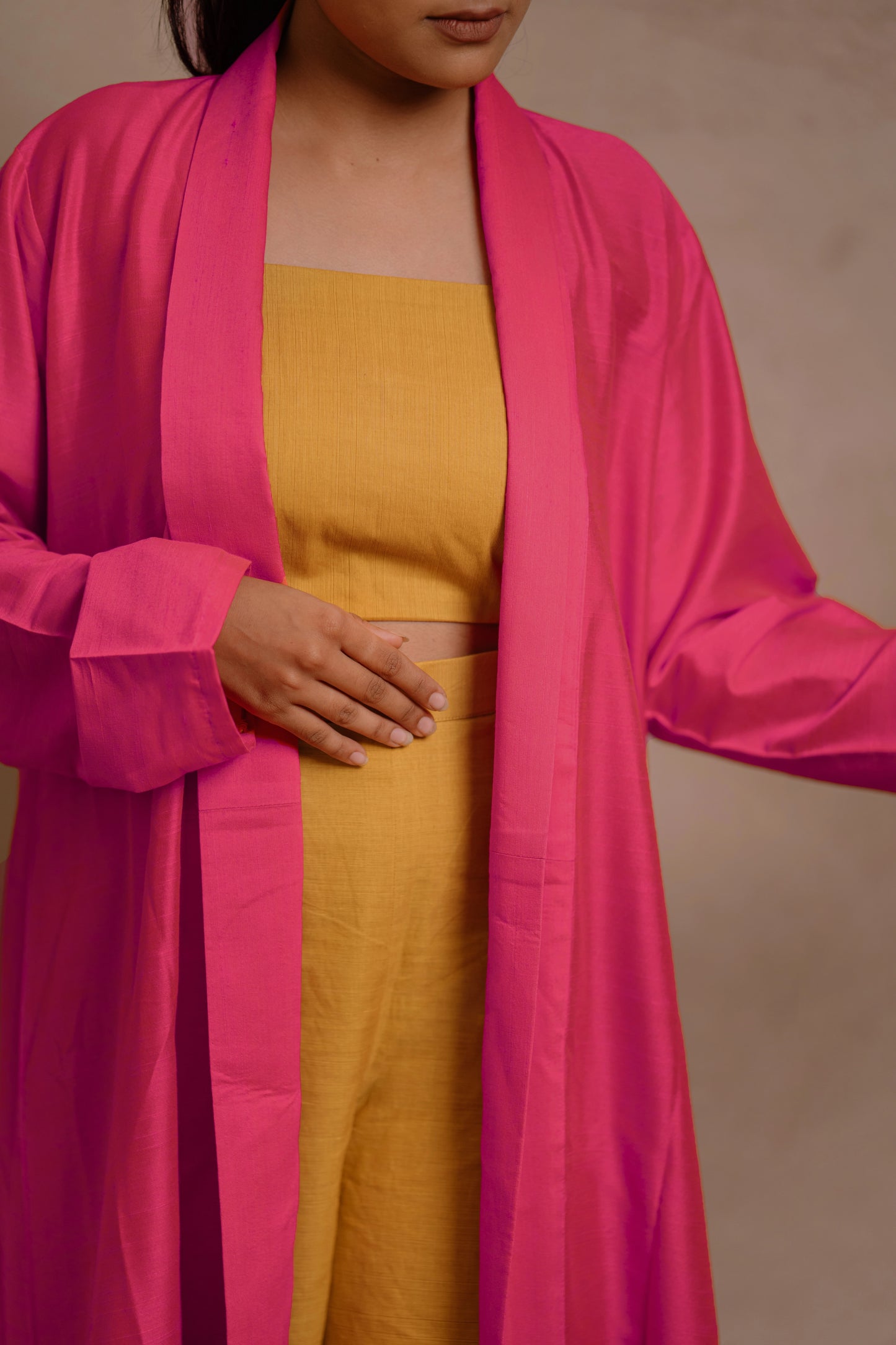 Model Krisha in a closeup in a long jacket in hot pink paired with a crop top & bell bottom pant in yellow by team AKloset.
