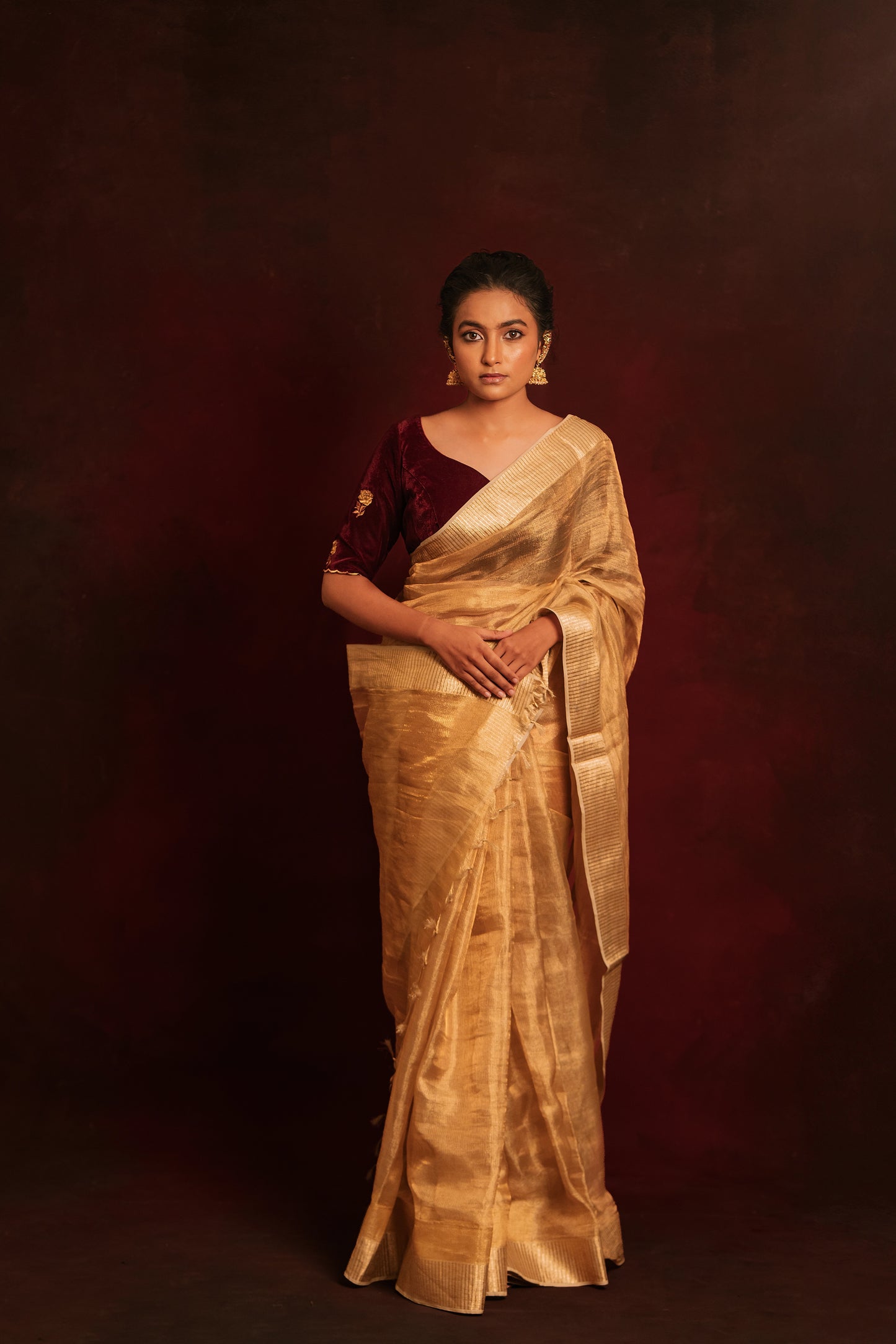 Model Krisha in a tissue saree in gold paired with an embroidered velvet blouse in dark maroon by team AKloset.