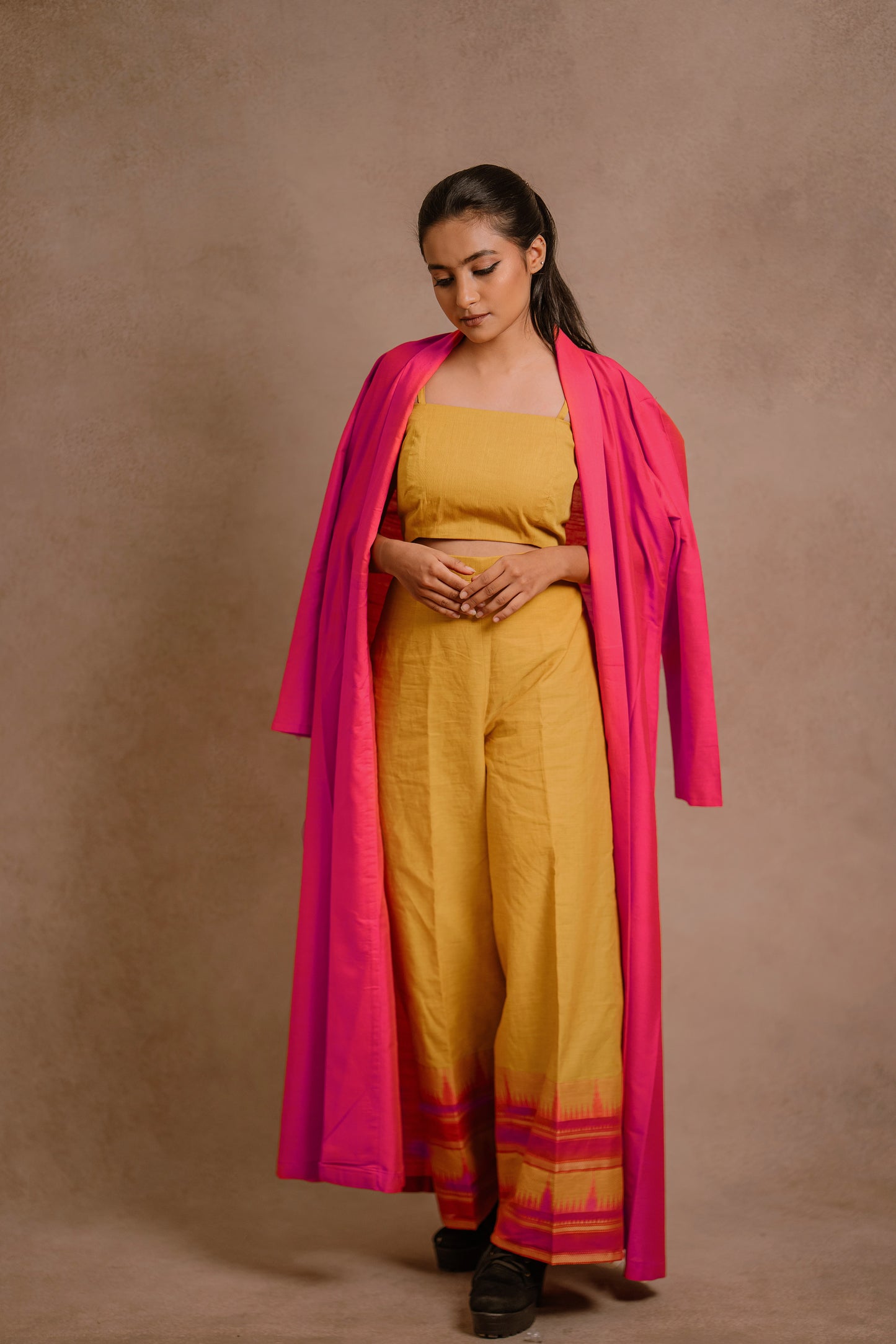 Model Krisha posing casually in a long jacket in hot pink paired with a crop top & bell bottom pant in yellow by team AKloset.