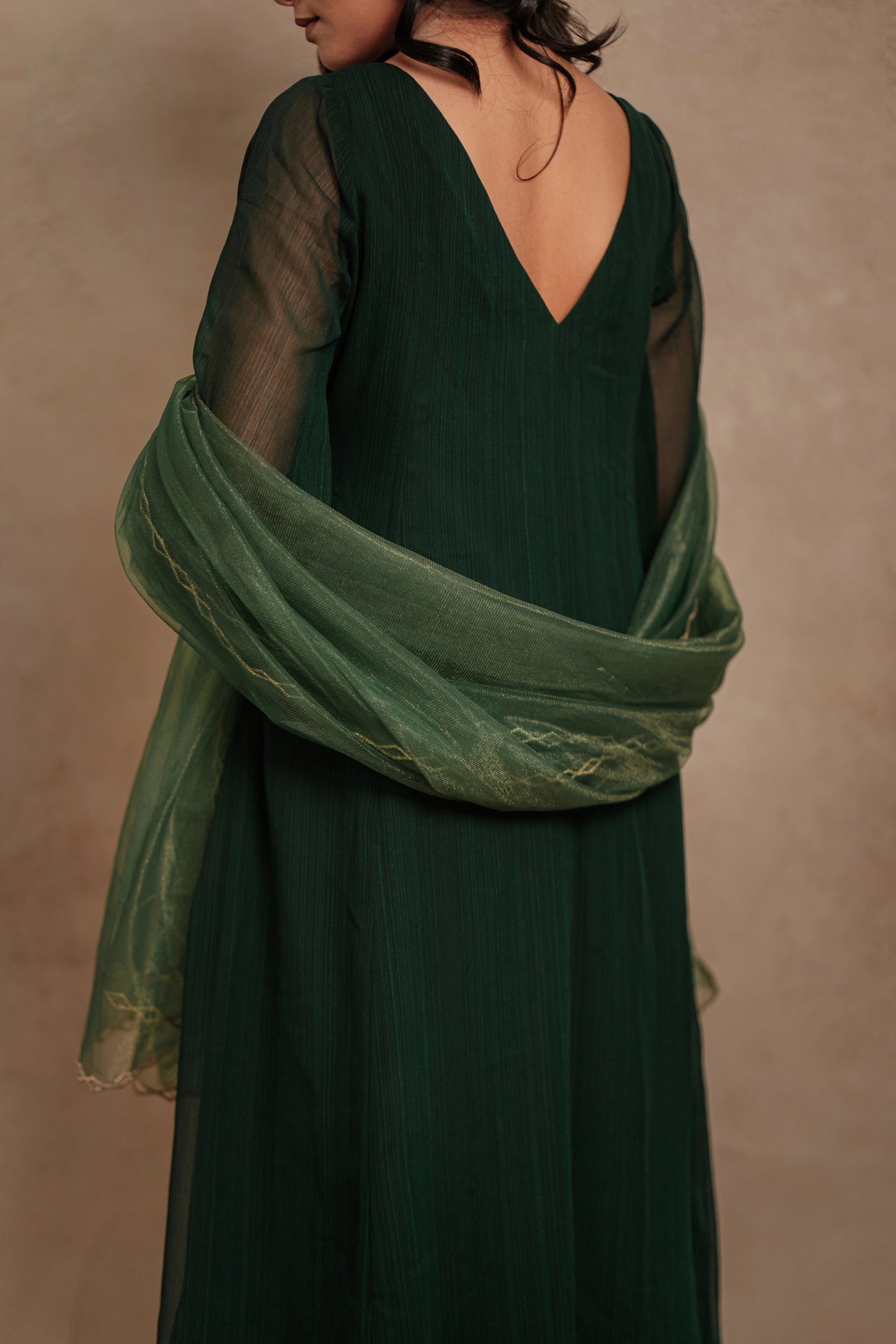 Model Krisha posing for back design in a hand embroidered tissue chiffon anarkali set in bottle green paired with a matching shimmer dupatta by team AKloset.