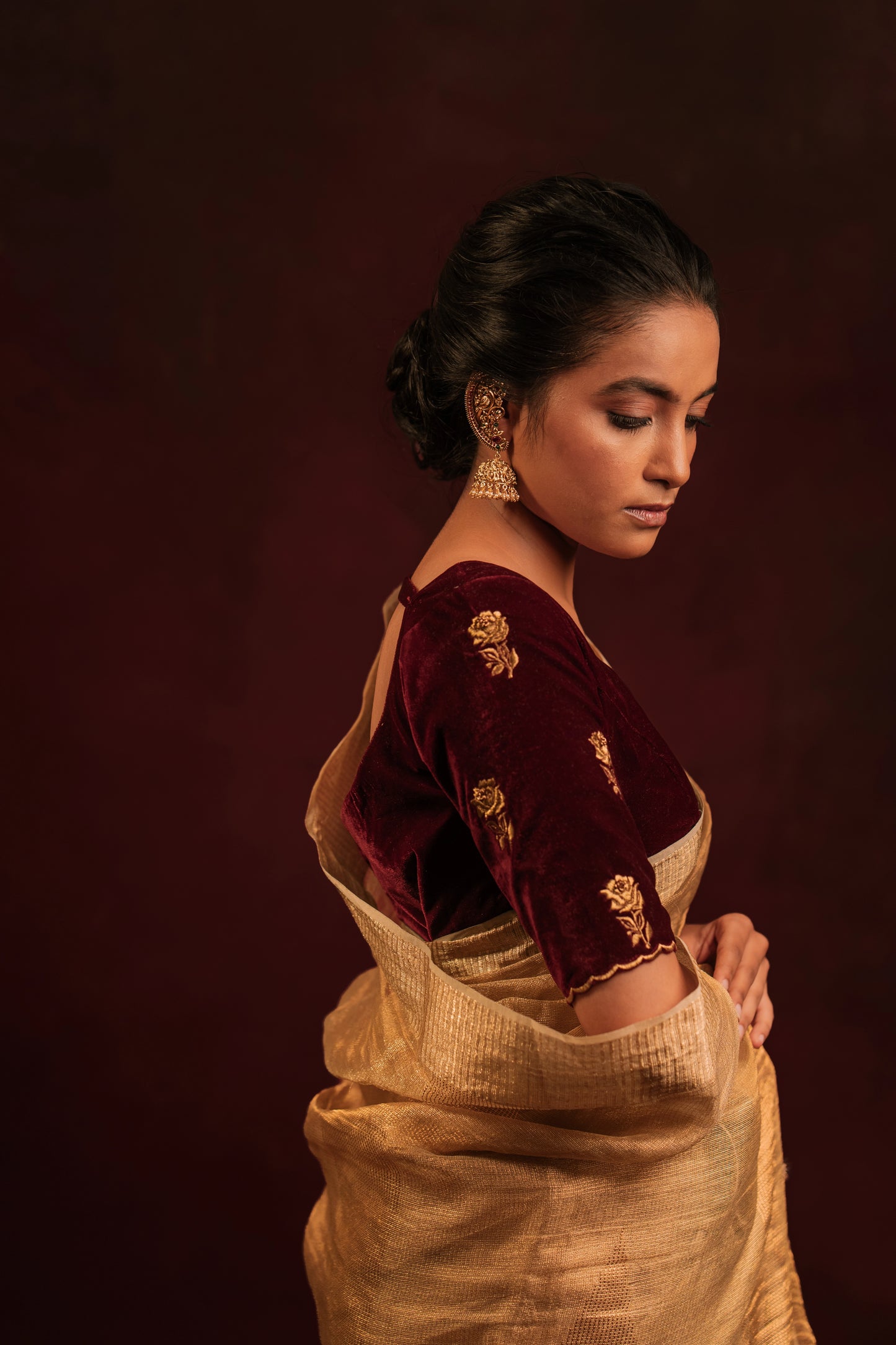 Model Krisha posing for detailing in a tissue saree in gold paired with an embroidered velvet blouse in dark maroon by team AKloset.