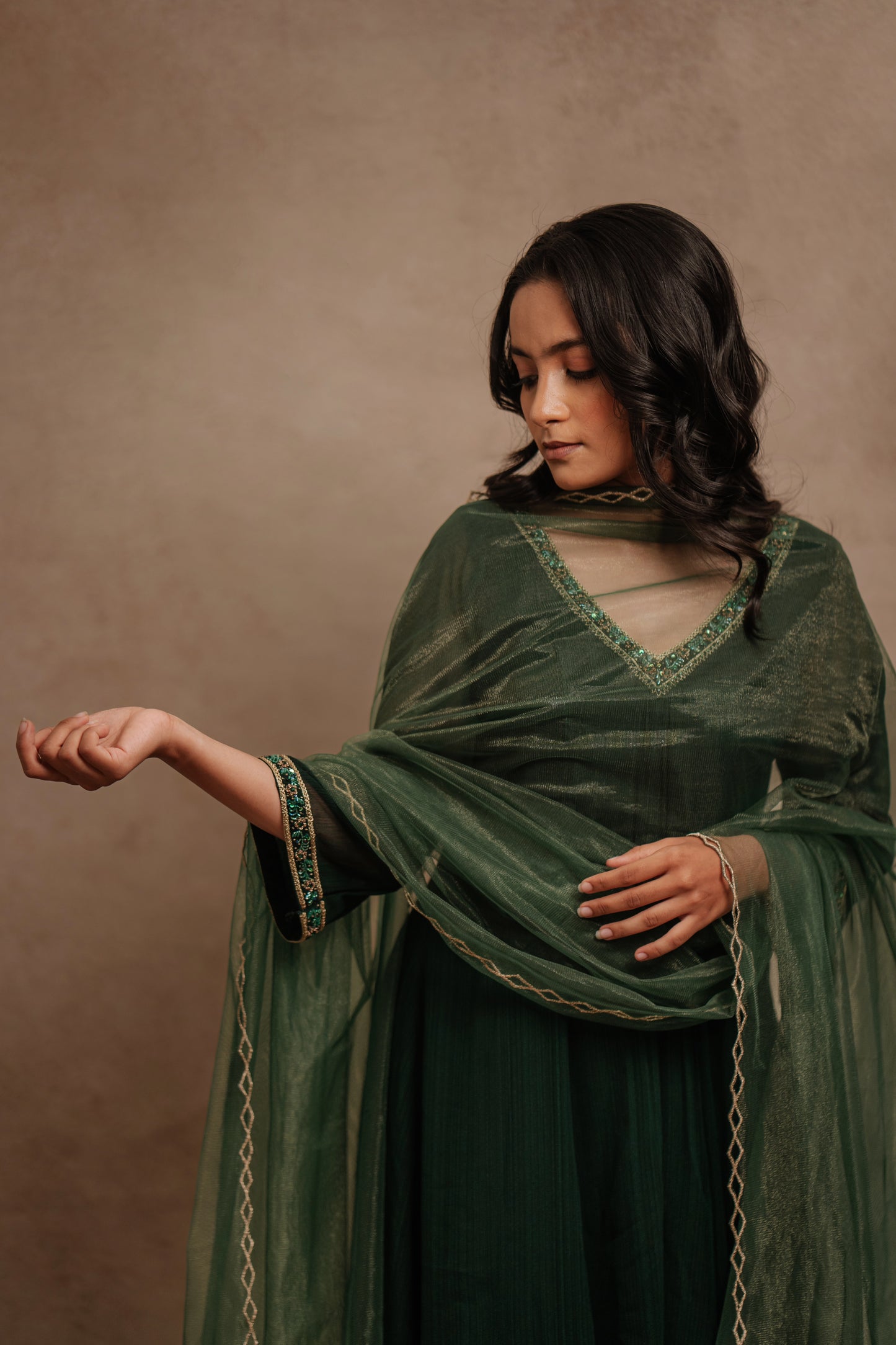 Model Krisha posing for photoshoot in a hand embroidered tissue chiffon anarkali set in bottle green paired with a matching shimmer dupatta by team AKloset.