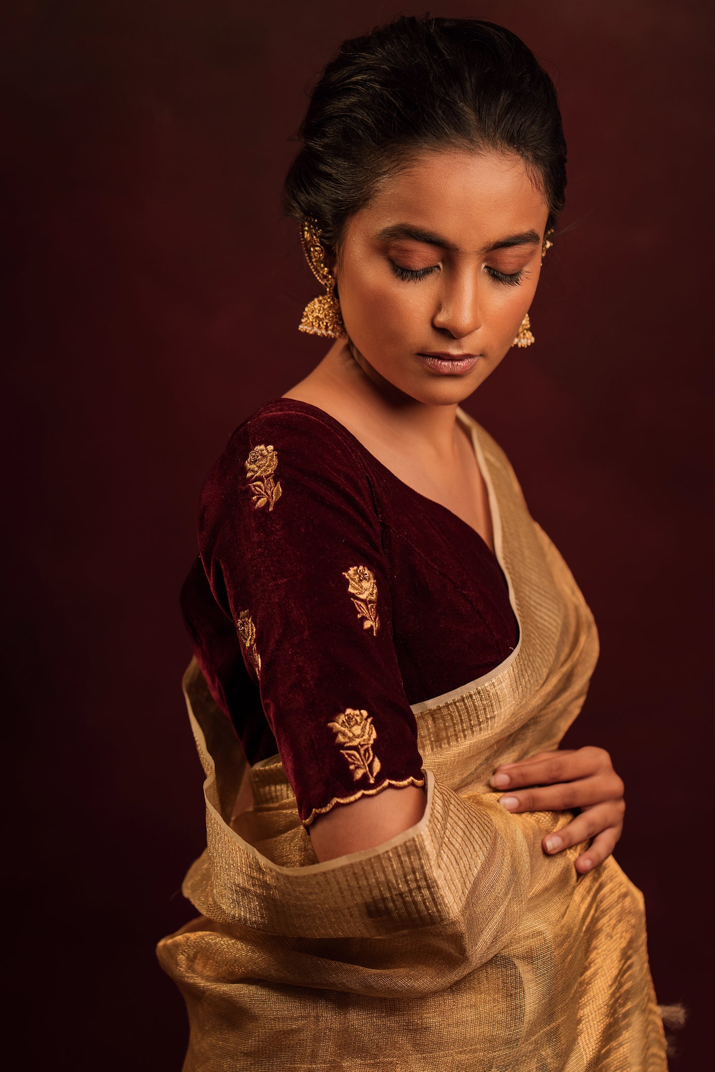 Model Krisha posing for sleeve in a tissue saree in gold paired with an embroidered velvet blouse in dark maroon by team AKloset.