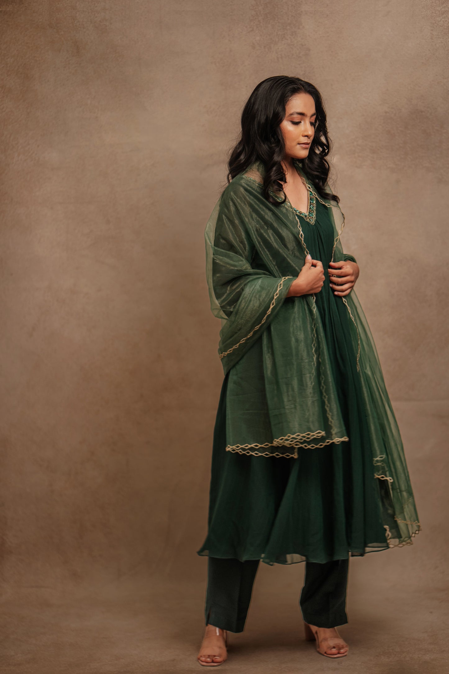 Model Krisha posing in a hand embroidered tissue chiffon anarkali set in bottle green paired with a matching shimmer dupatta by team AKloset.