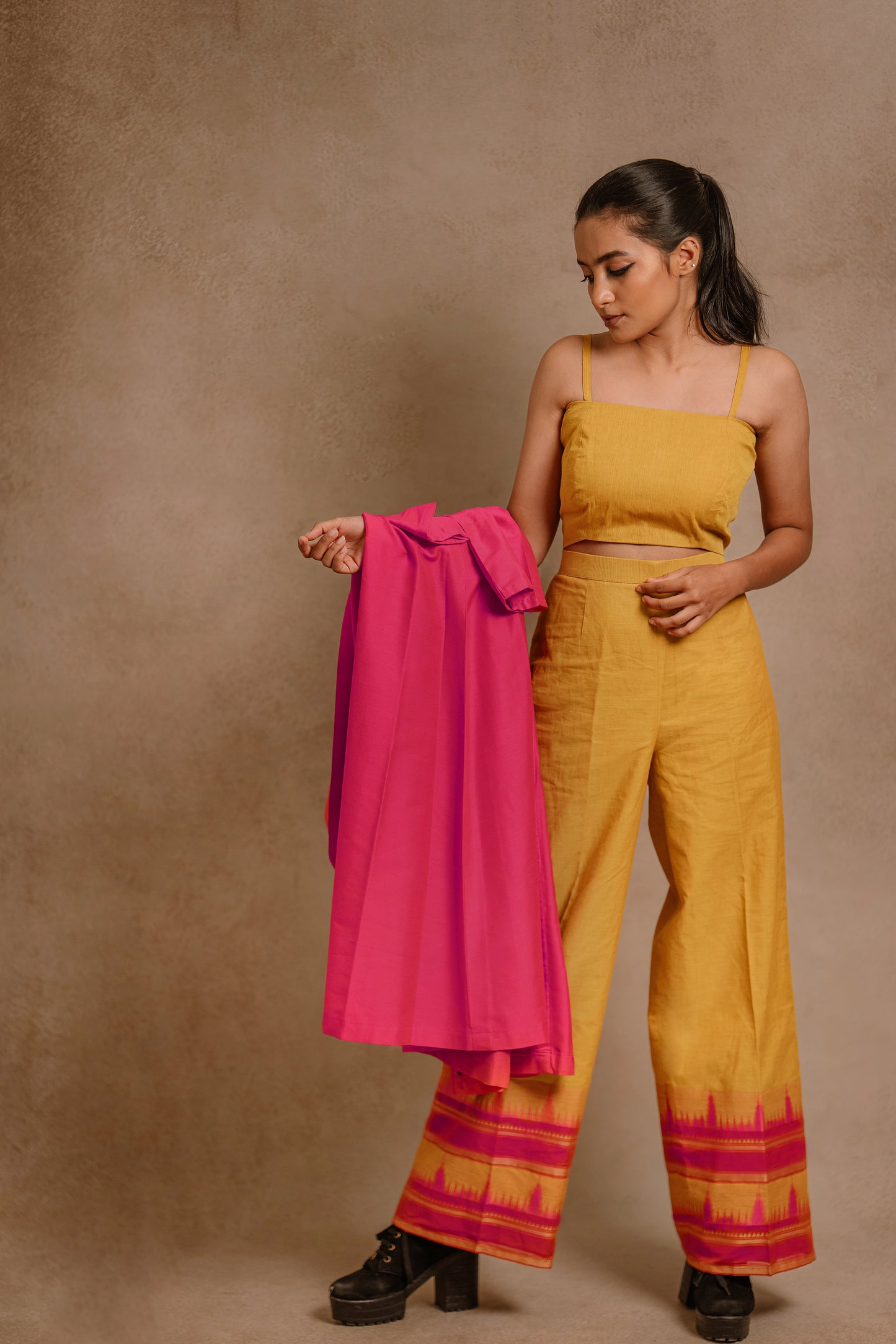 Model Krisha posing in a long jacket in hot pink paired with a crop top & bell bottom pant in yellow by team AKloset. Seen here without jacket.