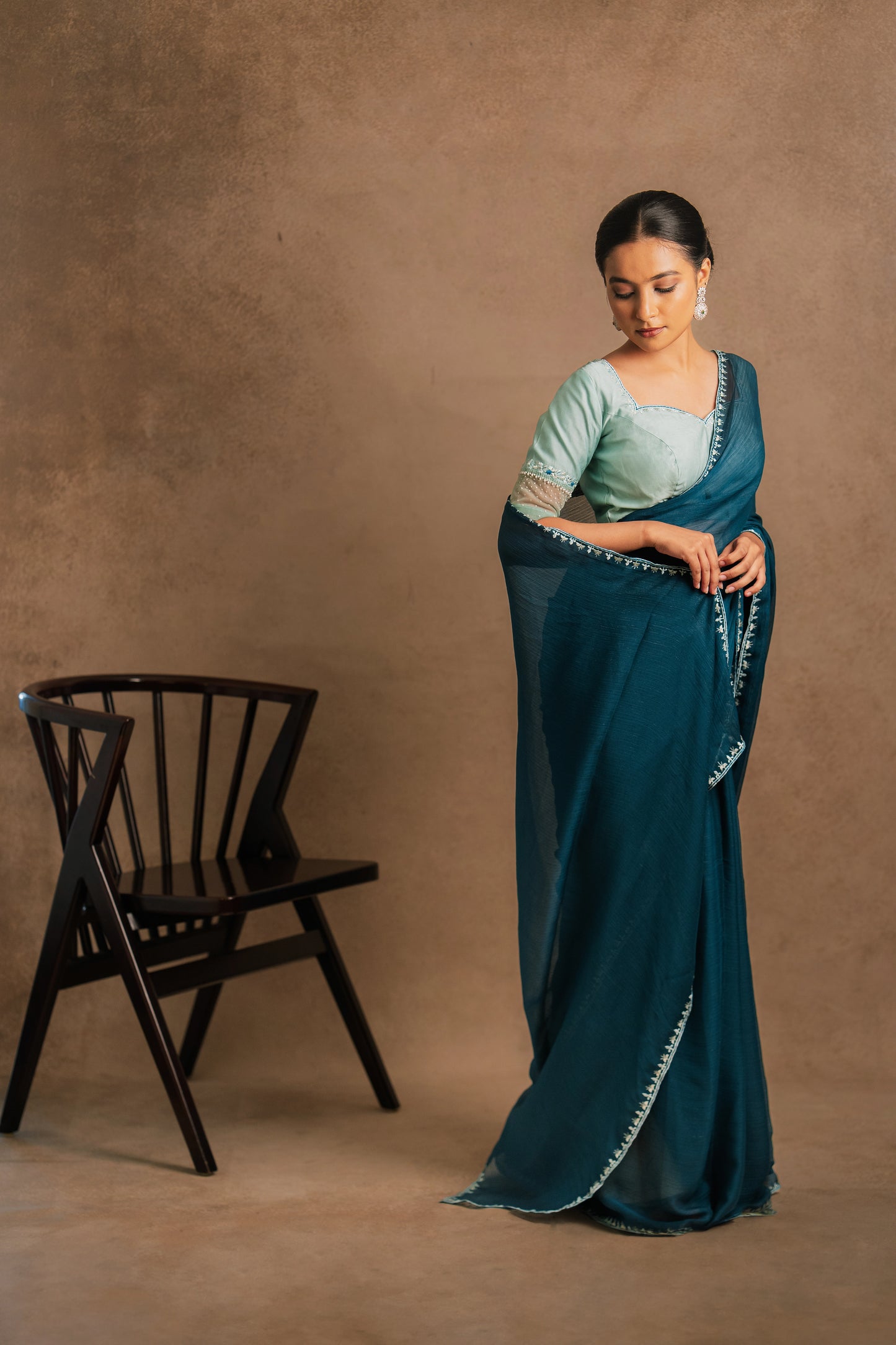 Model Krisha posing in a photoshoot in embroidered shimmer chiffon saree in teal paired with a chanderi blouse in muted turquoise with pearl beads detailing by team AKloset.