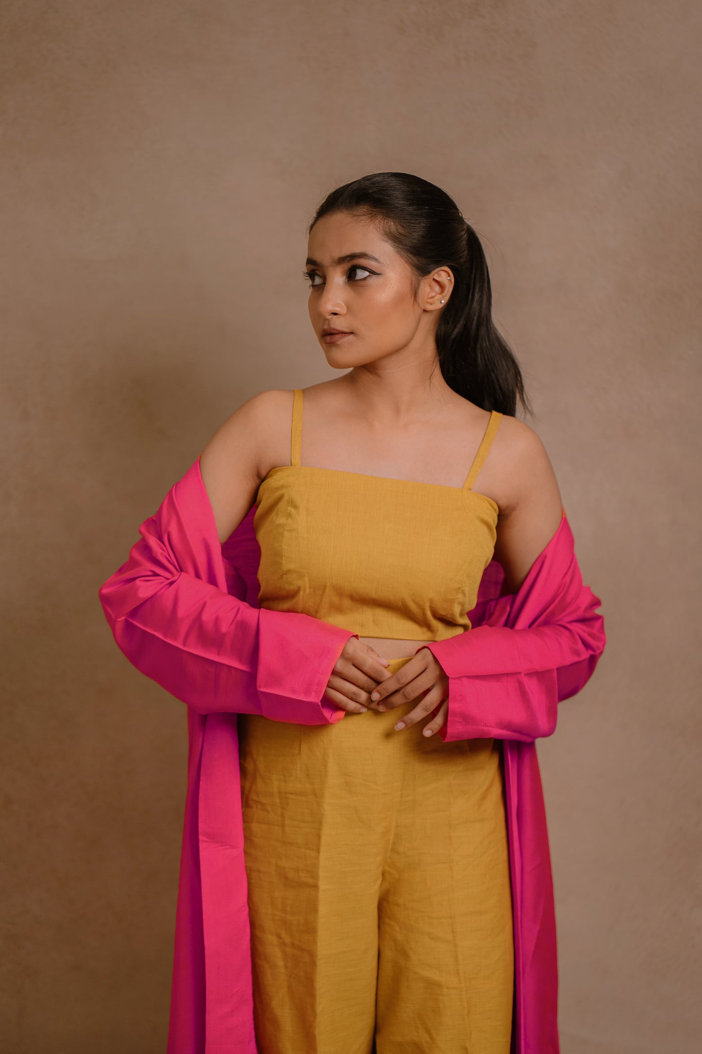 Model Krisha showcasing the top in a long jacket in hot pink paired with a crop top & bell bottom pant in yellow by team AKloset.