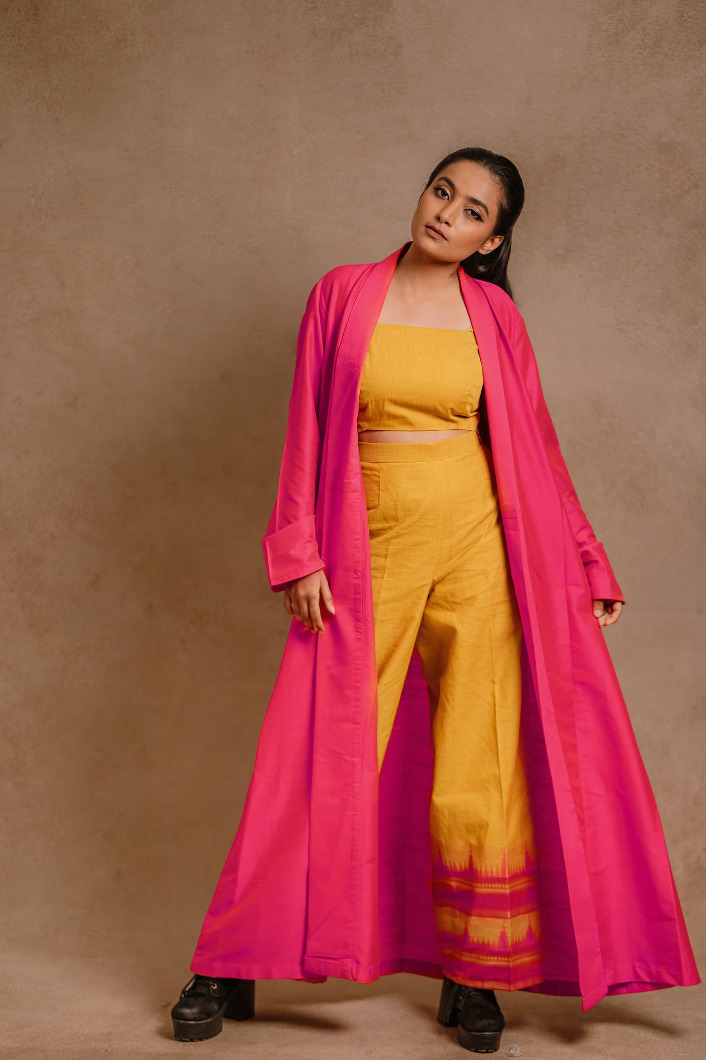 Model Krisha swaying in a long jacket in hot pink paired with a crop top & bell bottom pant in yellow by team AKloset.