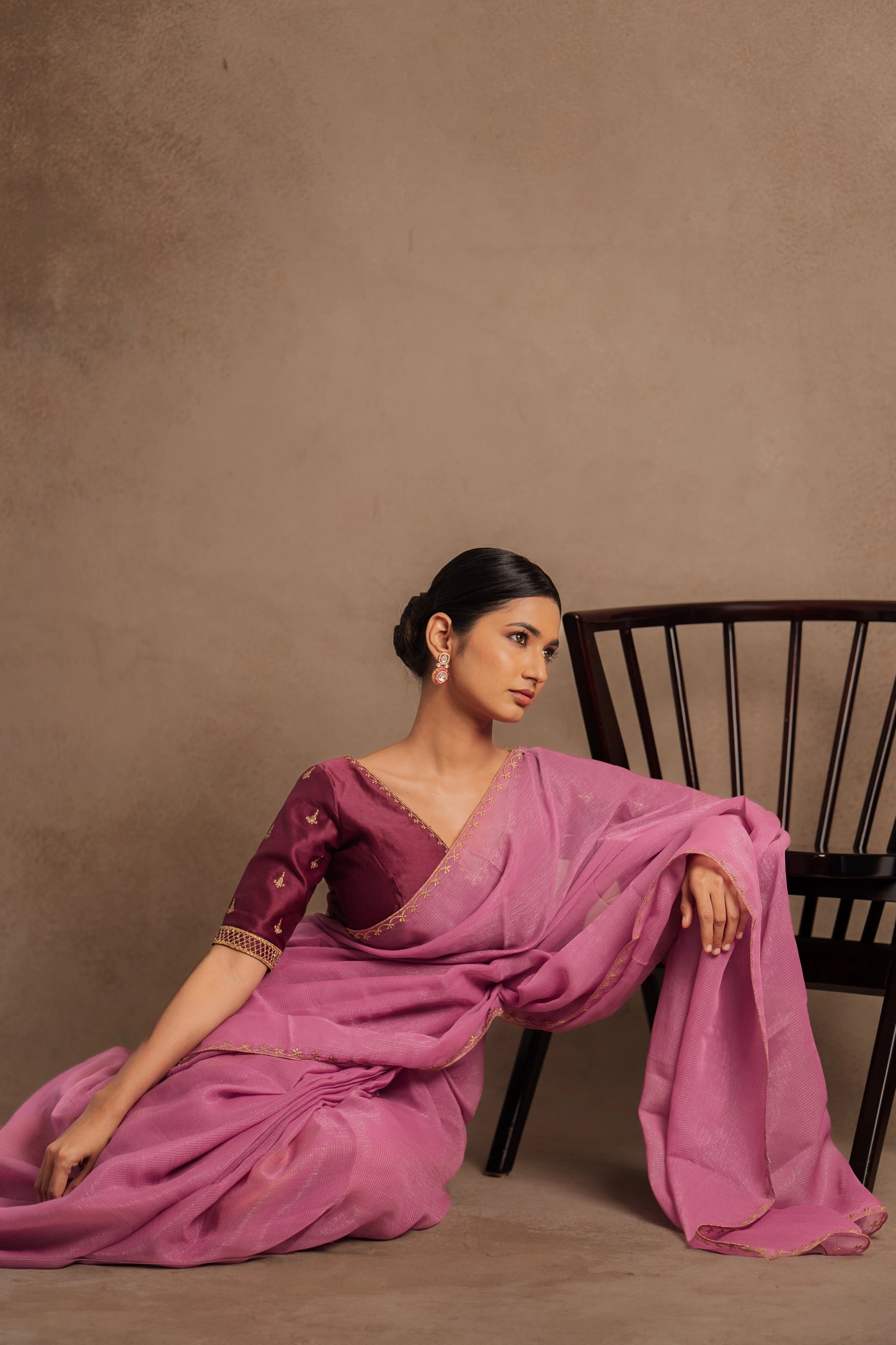 Model Premika Sekar in a seated pose in an embroidered Tissue Chiffon Saree in Onion Pink with an Embroidered Chanderi Blouse in Plum.