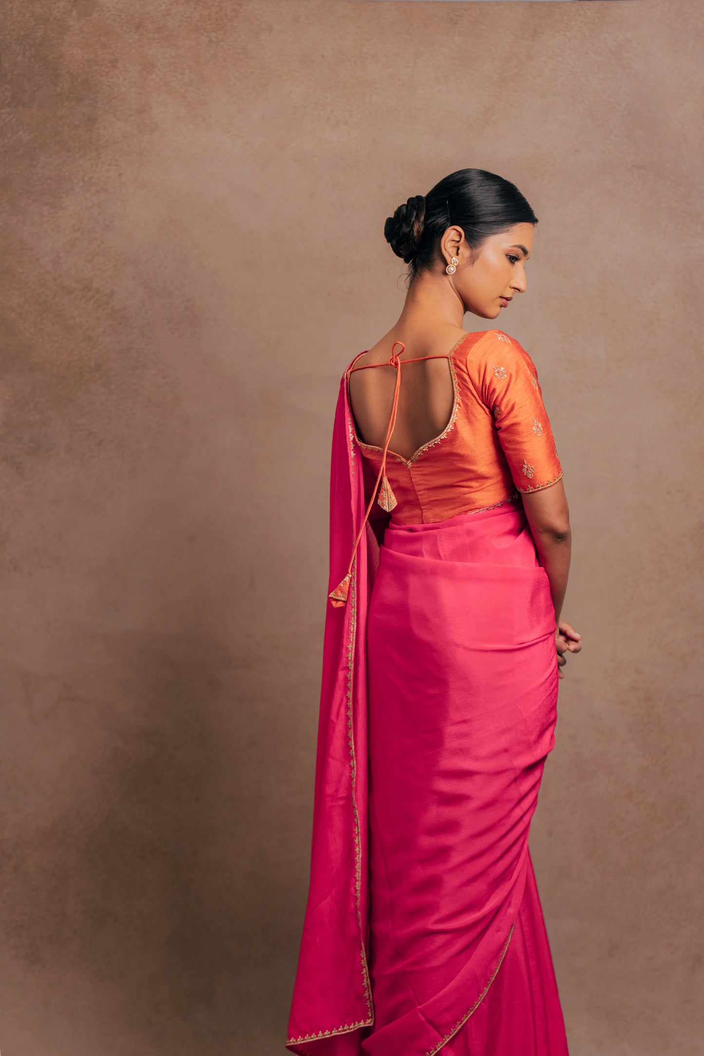 Model Premika Sekar posing during photoshoot for back blouse design in a pink shimmer chiffon saree paired with an embroidered orange raw silk blouse designed by team AKloset.