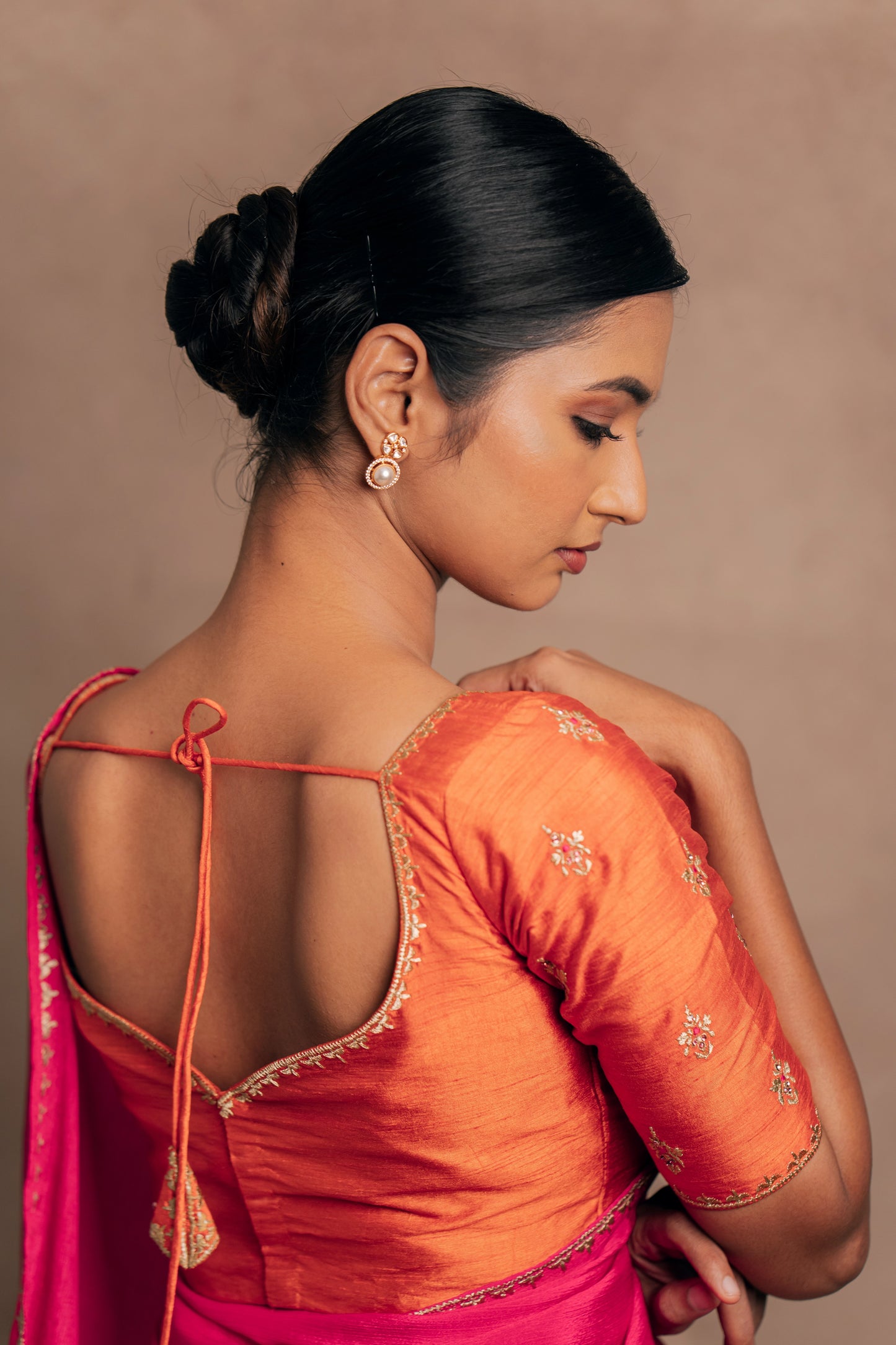 Model Premika Sekar posing for back blouse design in a pink shimmer chiffon saree paired with an embroidered orange raw silk blouse designed by team AKloset.