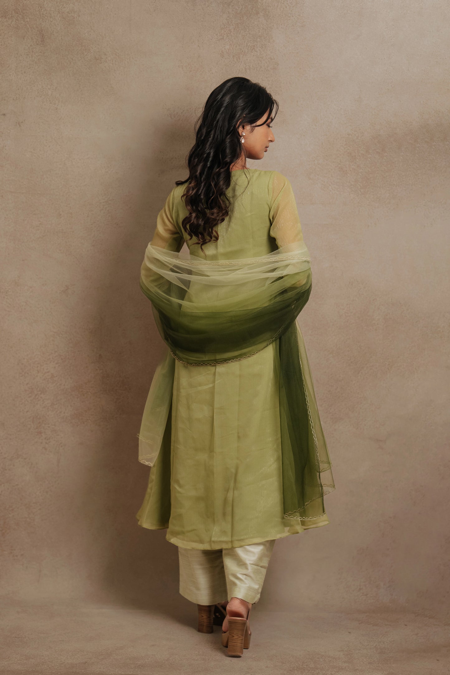 Model Premika Sekar posing for back design in an embroidered tissue chiffon salwar set in sage green, paired with a tulle dupatta in ombré by team AKloset.