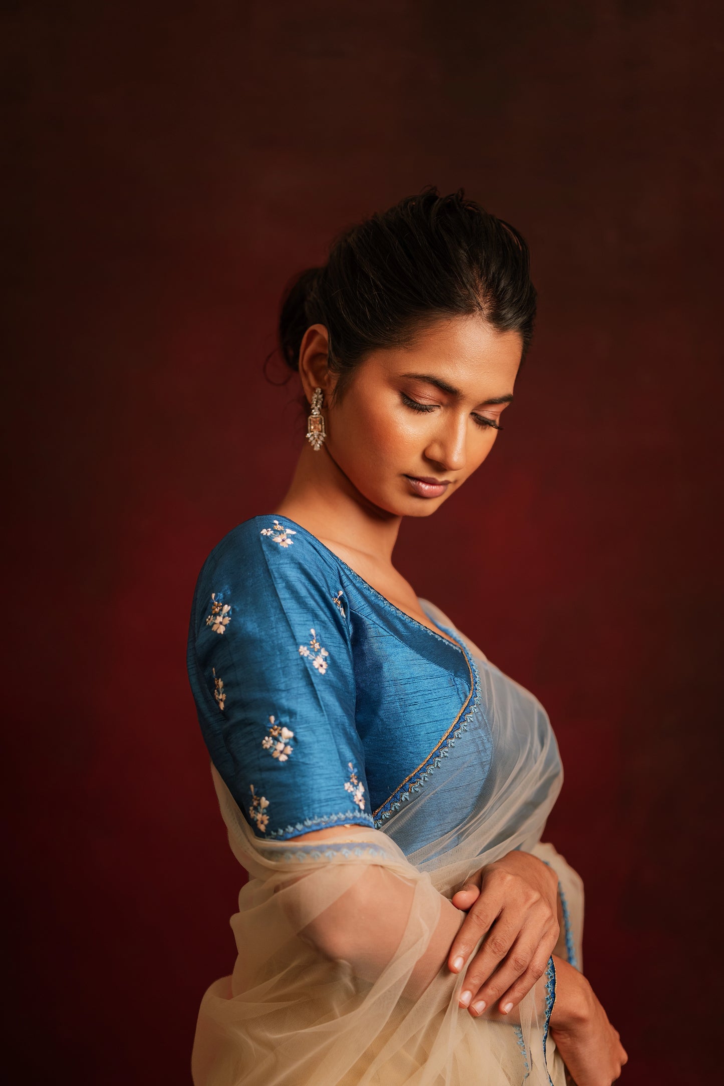 Model Premika Sekar posing for sleeve detailing in an ivory tulle saree embroidered with resham paired with an embroidered rawsilk blouse in cerulean blue by team AKloset.