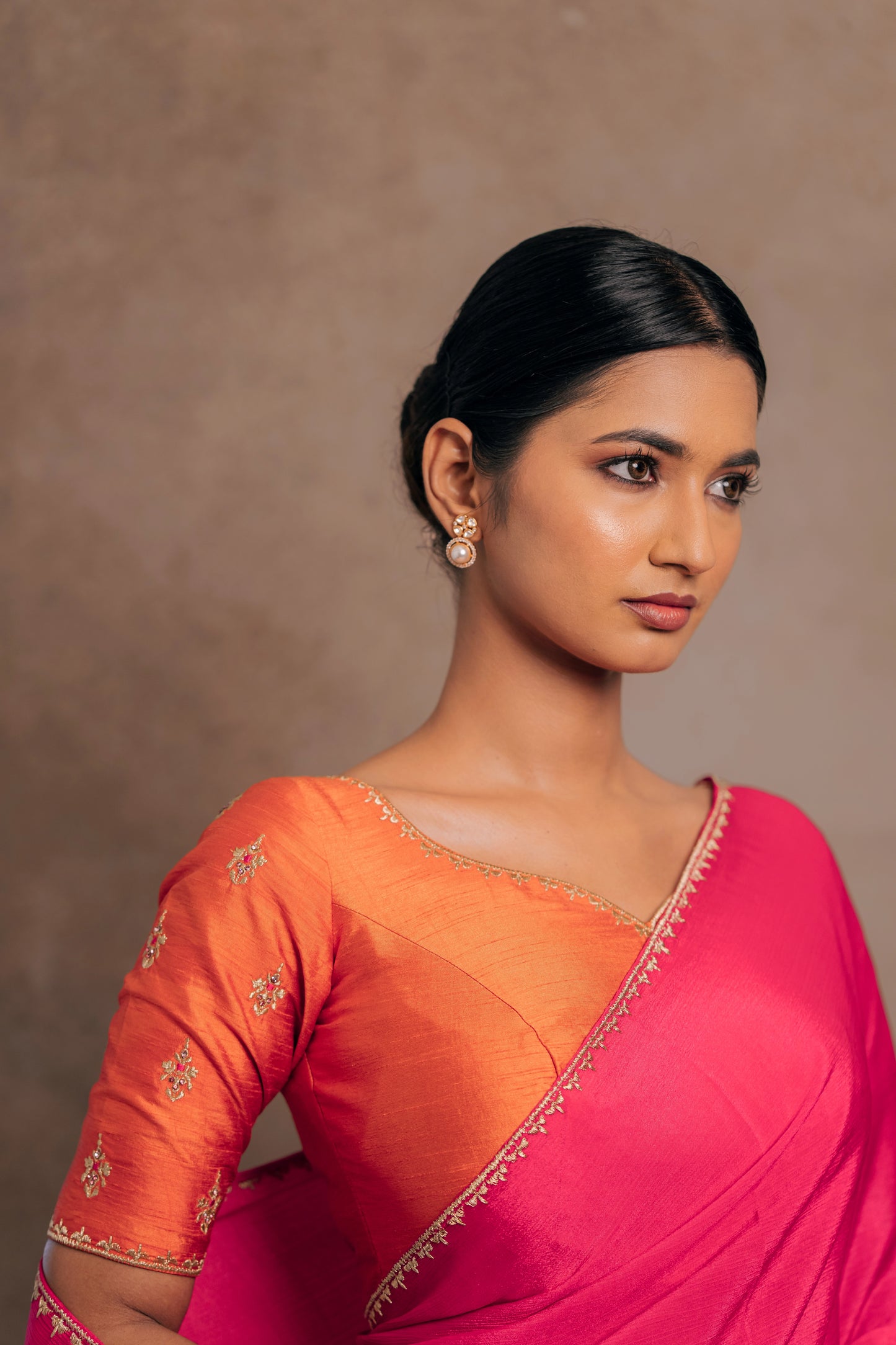 Model Premika Sekar posing in a pink shimmer chiffon saree paired with an embroidered orange raw silk blouse designed by team AKloset.