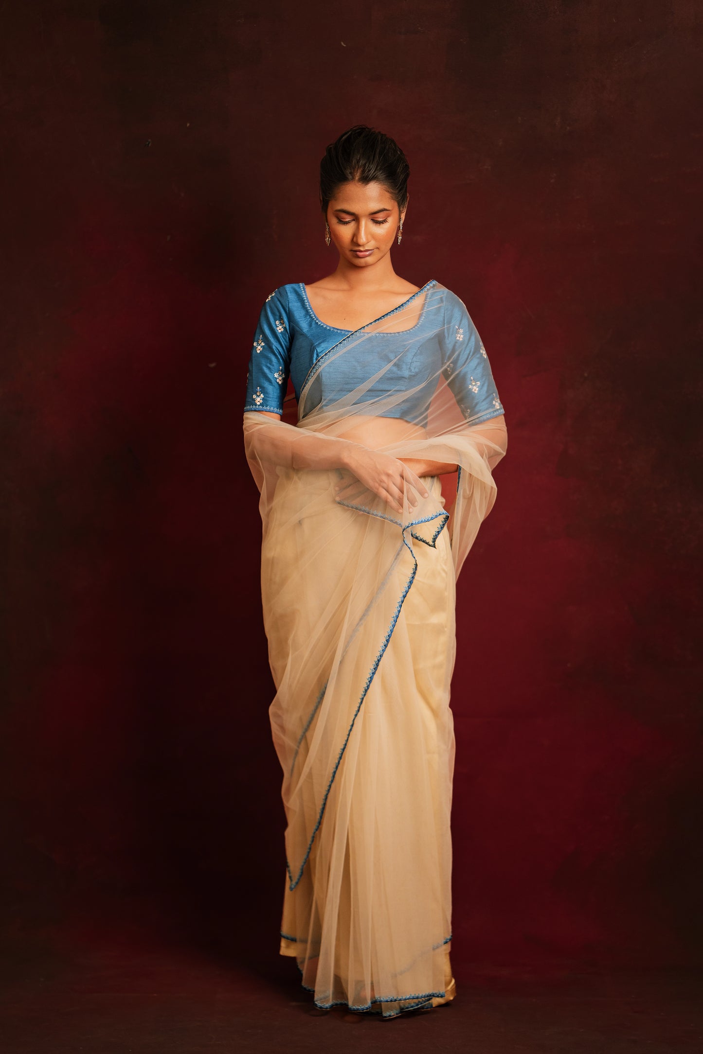Model Premika Sekar posing in an ivory tulle saree embroidered with resham paired with an embroidered rawsilk blouse in cerulean blue by team AKloset.
