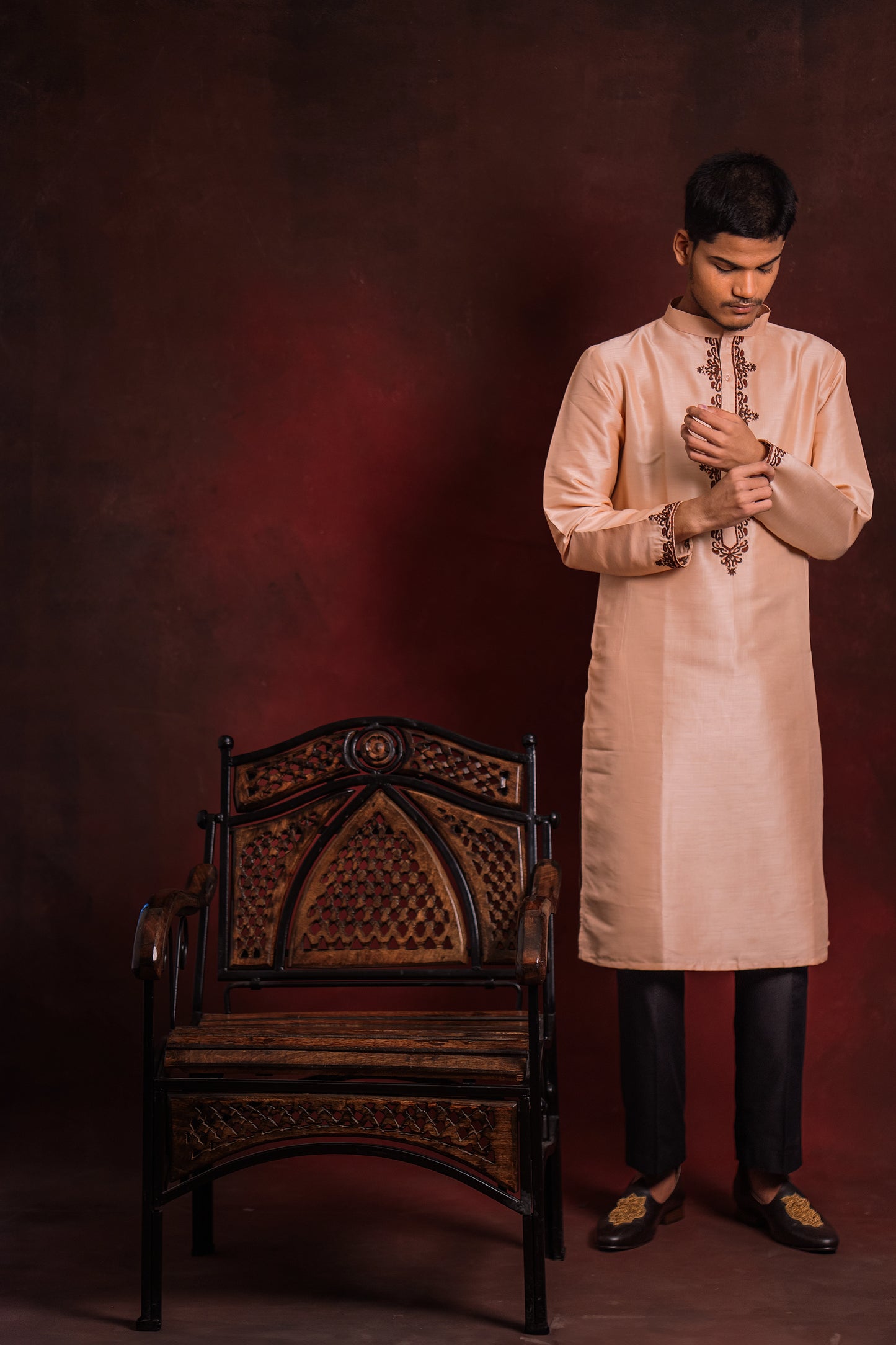 Model in a light pink kurta with intricate embroidery by team AKloset standing next to a wooden chair against a dark background.