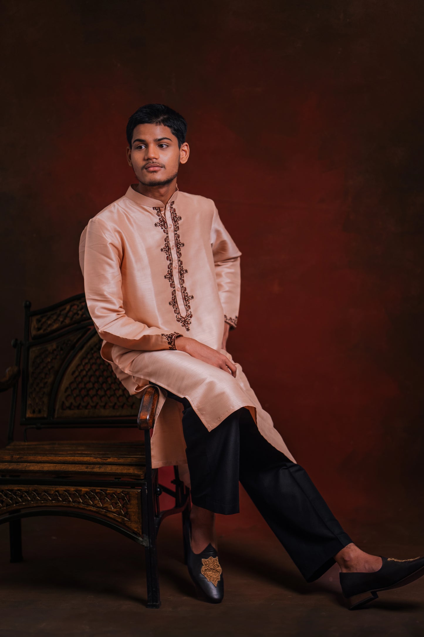 Model poses on a chair in a light pink kurta with intricate embroidery by team AKloset.